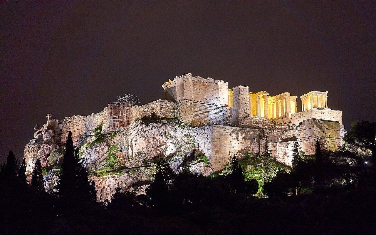 Classical columned temples illuminated on a rocky hill above a city at dusk