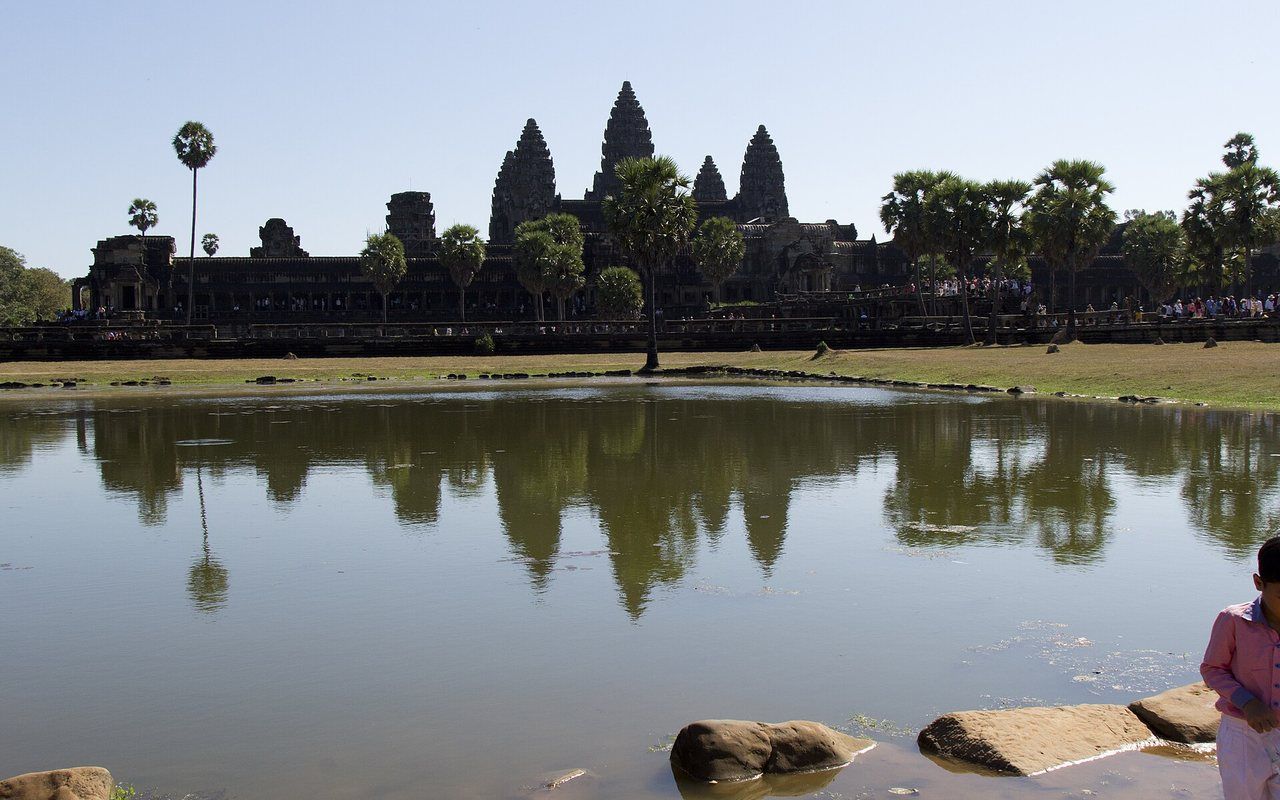 Stone temple towers beyond a reflecting pool, grass, and palm trees