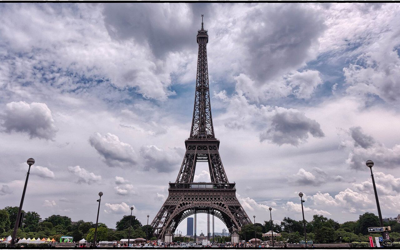 A tall iron lattice tower rising above trees and a broad city skyline