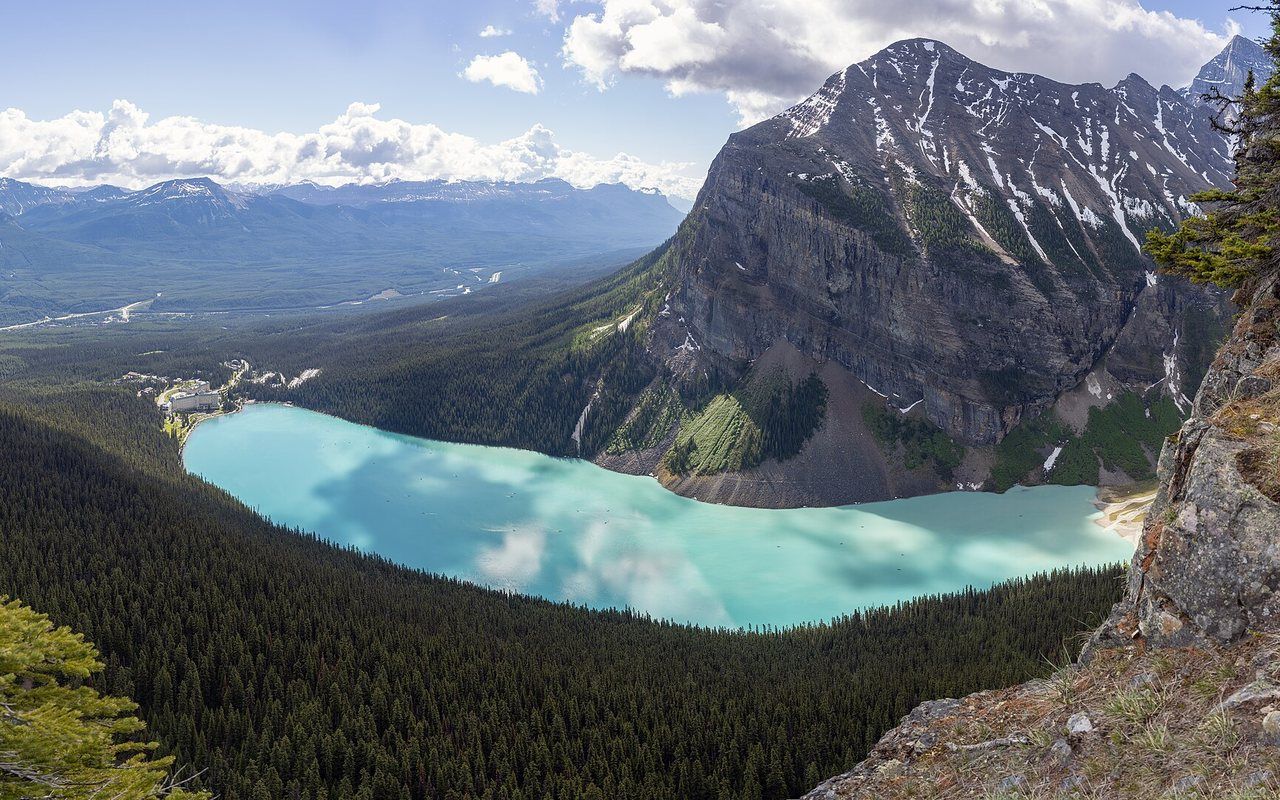 A turquoise glacial lake below snowy peaks and dark evergreen forest