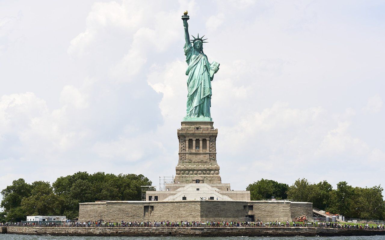 A giant green copper figure holding a torch on an island in a wide harbor