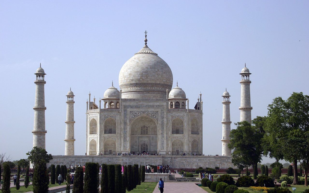 A white marble mausoleum with a central dome reflected in a long garden pool